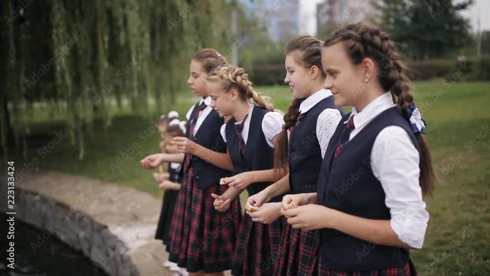 Students in school uniform feeding ducks in a pond in the school yard. Girls College coeds wearing the same school uniform feed the ducks in the pond on campus