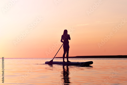 Silhouette of a beautiful woman on SUP surfing.