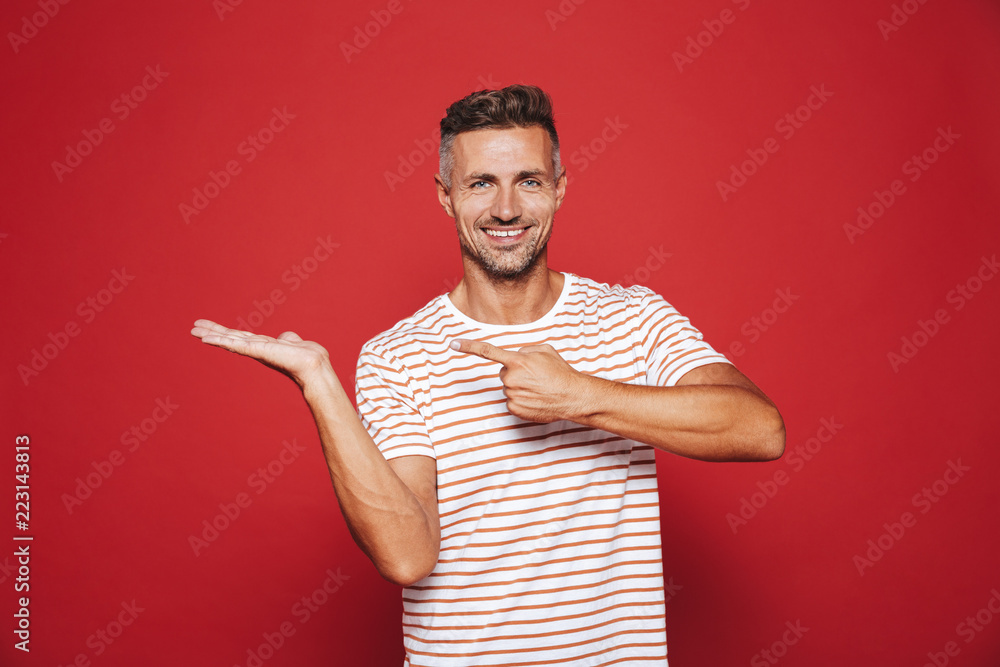 Unshaved guy in striped t-shirt gesturing index fingers at copyspace on his palm, isolated over red background Unshaved guy in striped t-shirt gesturing index fingers at copyspace on his palm, isolated over red background