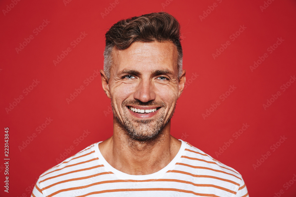 Happy attractive man with stubble in striped t-shirt smiling on camera, isolated over red background Happy attractive man with stubble in striped t-shirt smiling on camera, isolated over red background
