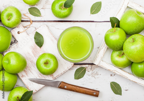 Glass of fresh organic apple juice with granny smith green apples in box on wooden background with knife photo