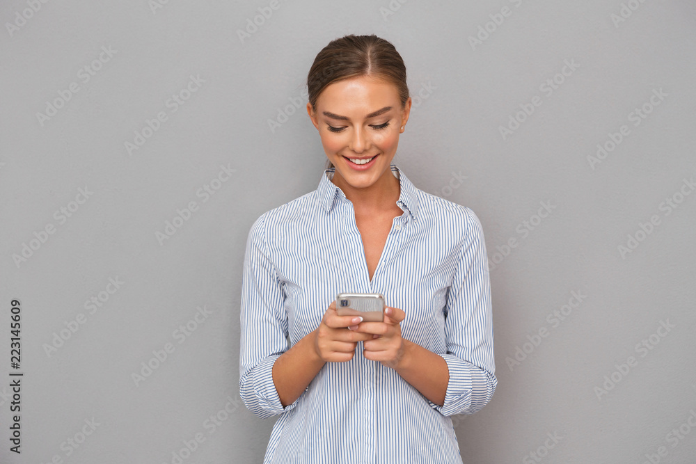 Smiling business woman standing over grey wall background using mobile phone. Smiling business woman standing over grey wall background using mobile phone.