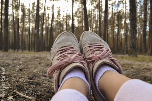 A female feet in sneakers against a forest background. A girl relaxing in the forest.