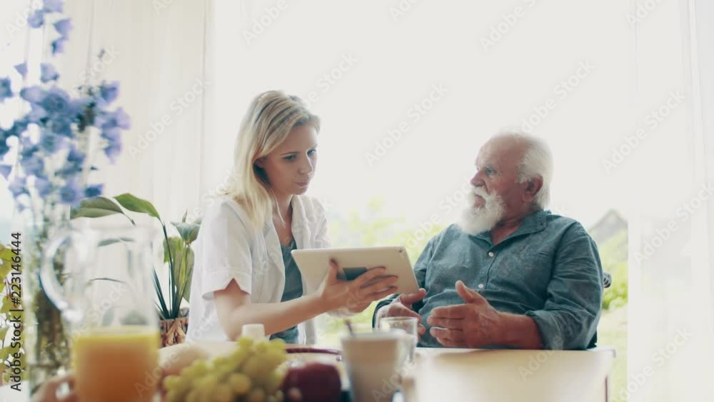 Health visitor with tablet and a senior man in wheelchair at home, talking. Health visitor with tablet and a senior man in wheelchair at home, talking.