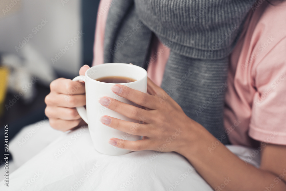 cropped shot of sick woman in bed holding cup of hot tea cropped shot of sick woman in bed holding cup of hot tea