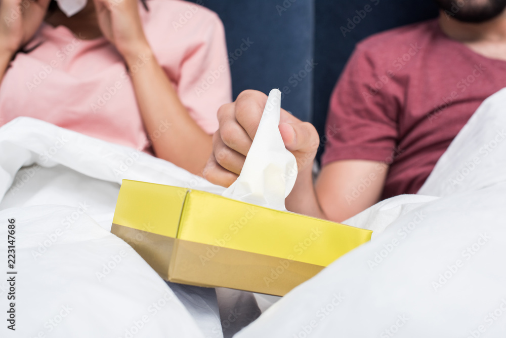 cropped shot of sick couple sitting in bed and taking paper napkins out of box cropped shot of sick couple sitting in bed and taking paper napkins out of box