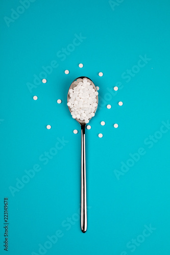 Sugar substitute pills in a spoon, on a blue background