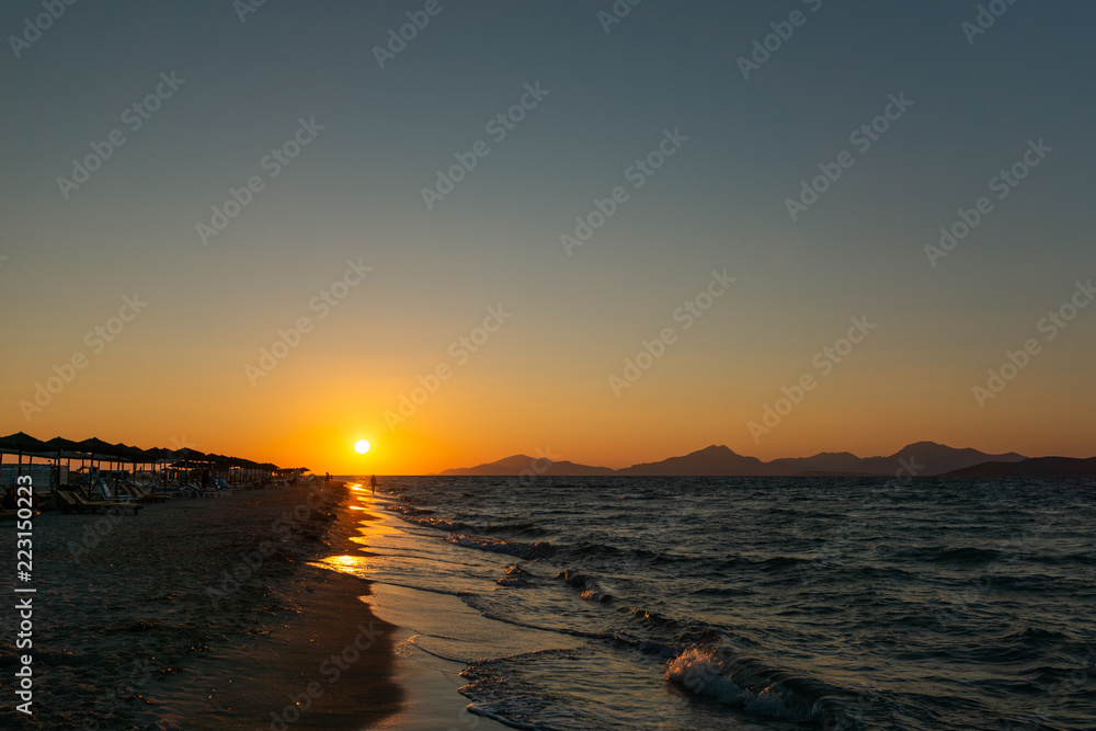 Dramatischer Sonnenuntergang mit Meer, Bergen und Sonnenschirmen