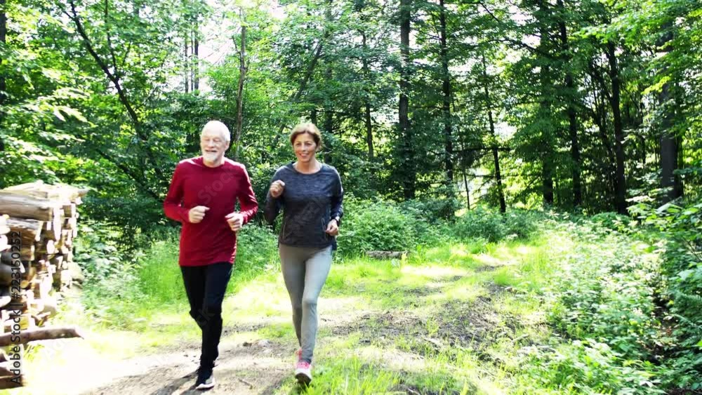 Senior sporty couple running in the forest outdoors in sunny nature. Senior sporty couple running in the forest outdoors in sunny nature.