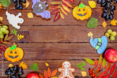 Beautiful festive background for Halloween with gingerbread, autumn leaves, berries and candy on a wooden table. Free space