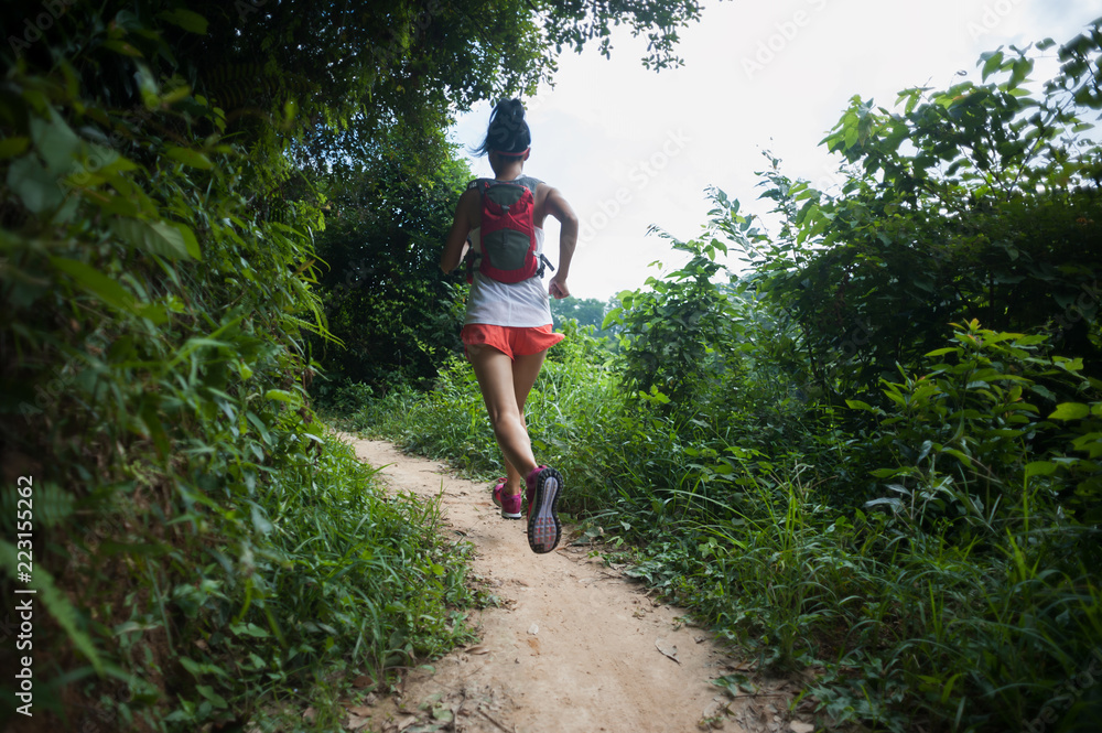 Young woman trail runner running on tropical forest trail Young woman trail runner running on tropical forest trail