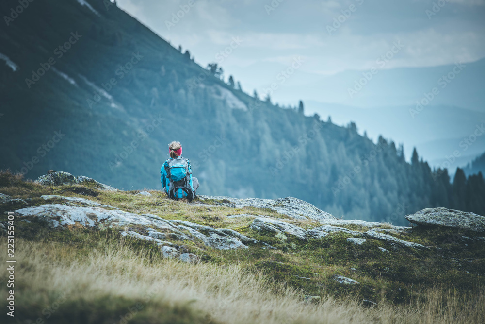 Junge blonde Frau sitzend in den Bergen, Blick in die Ferne, Abenteuer