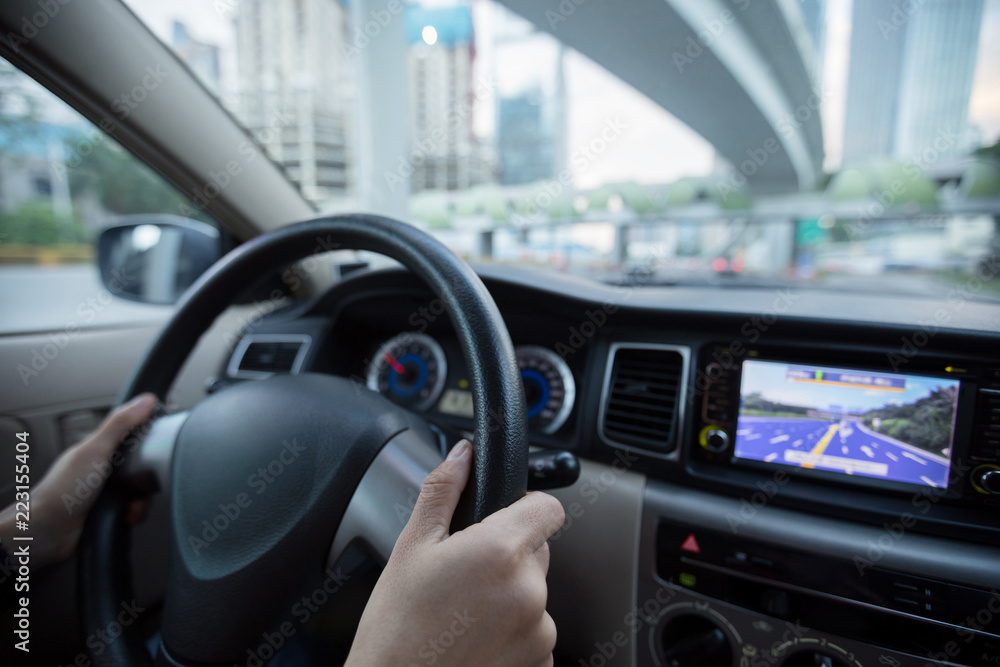 Hands holding steering wheel while driving car on city road