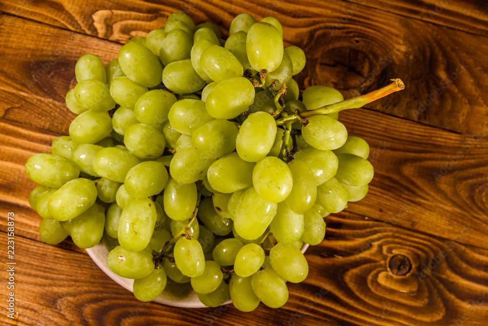 Ceramic plate with green grapes on wooden table. Top view Ceramic plate with green grapes on wooden table. Top view