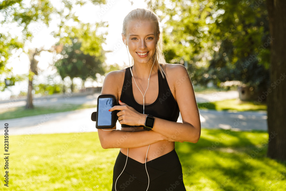 Blonde sports woman in park outdoors using mobile phone listening music. Blonde sports woman in park outdoors using mobile phone listening music.