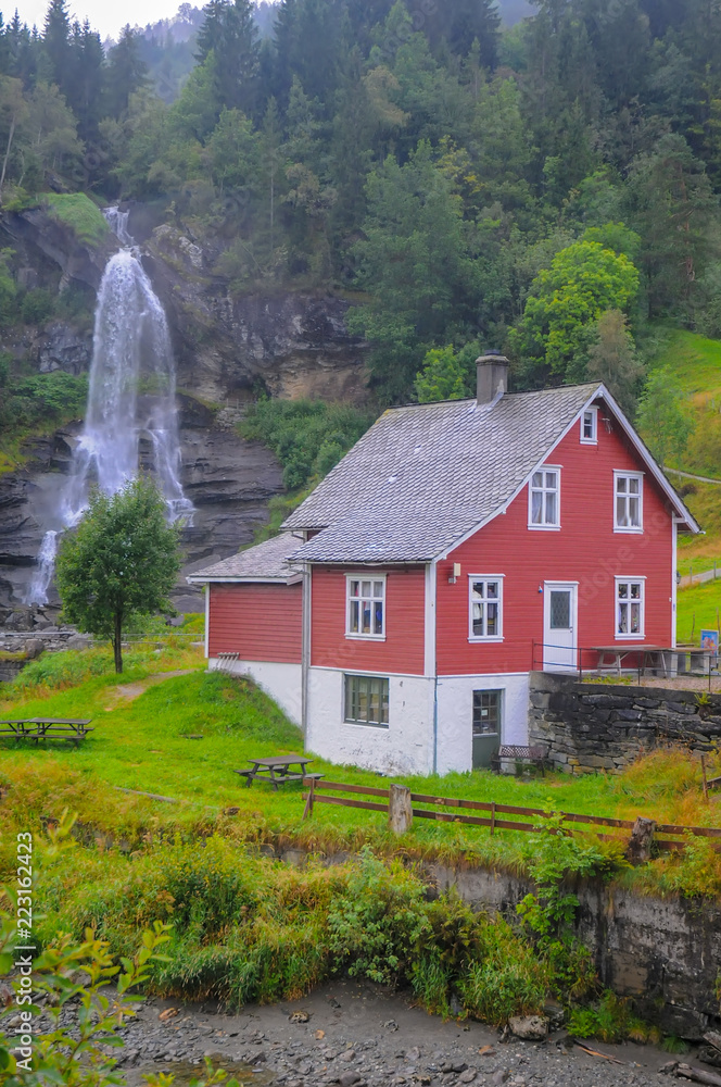 Traditional norwegian red wooden house and Steinsdalsfossen waterfall in the background, Norway