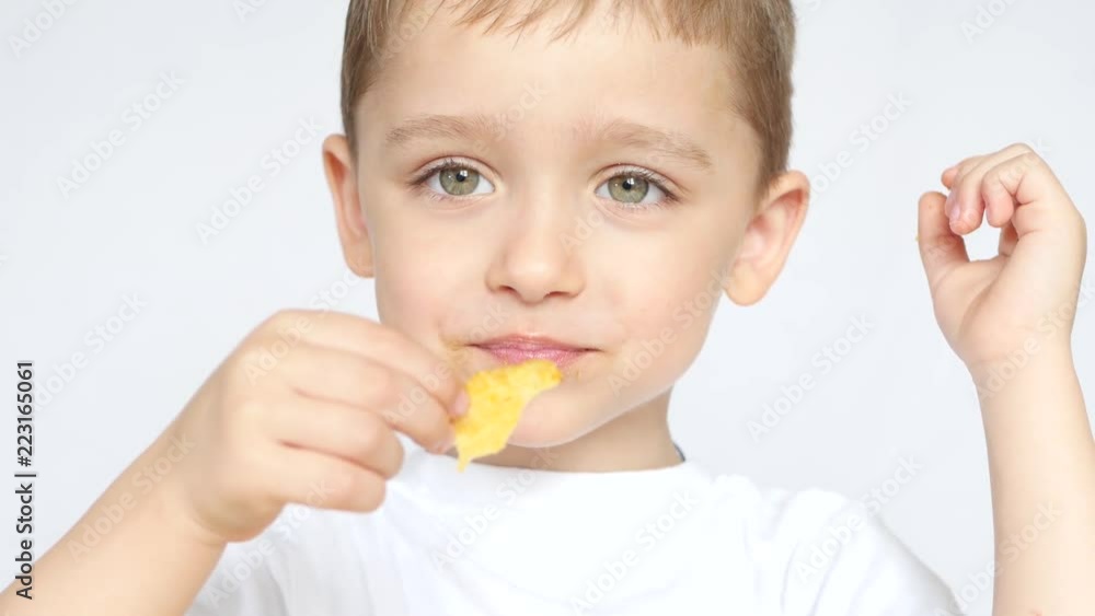 A child with pleasure and delight eats potato chips sitting at a table on a white background. Close-up A child with pleasure and delight eats potato chips sitting at a table on a white background. Close-up