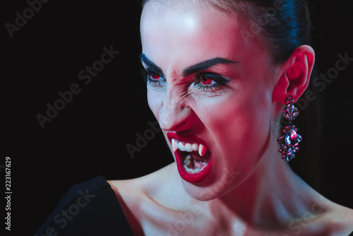 dreadful vampire showing her fangs and looking away isolated on black