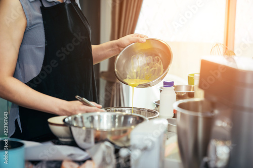 Asian women are mixing the ingredients of a cake in a stainless bowl in her kitchen for weekend party.