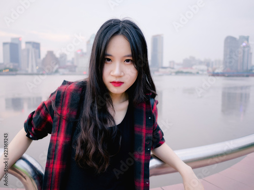 Outdoor portrait of young Chinese girl in black and red shirt with shanghai bund skyline background, travel and lifestyle concept.