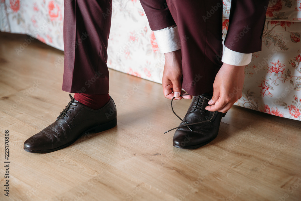 Close-up hands of a man tie laces on black shoes. A businessman in burgundy trousers and socks wears shoes before going to work in the office. The concept of fashion clothing and shoes.