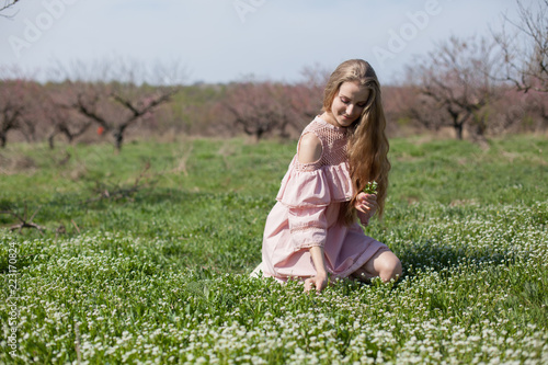 blonde woman in pink dress walks in the garden and gathers flowers