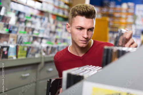 Male choosing CD with interesting movies on shelves in store