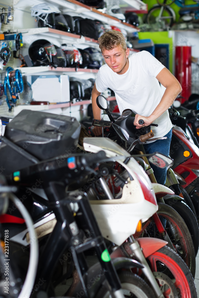 Young attentive man motorcyclist choosing the bike in the shop