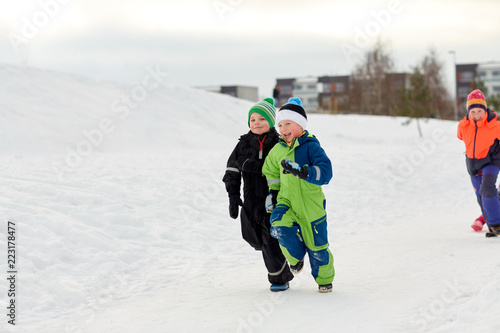 childhood, leisure and season concept - group of happy little kids in winter clothes running outdoors