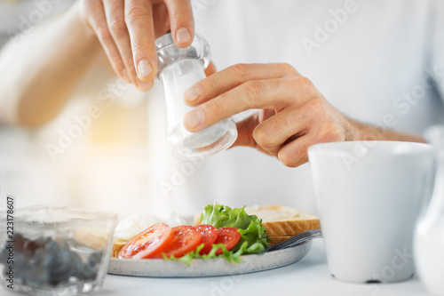 food, eating and people concept - close up of male hands seasoning breakfast by salt mill photo