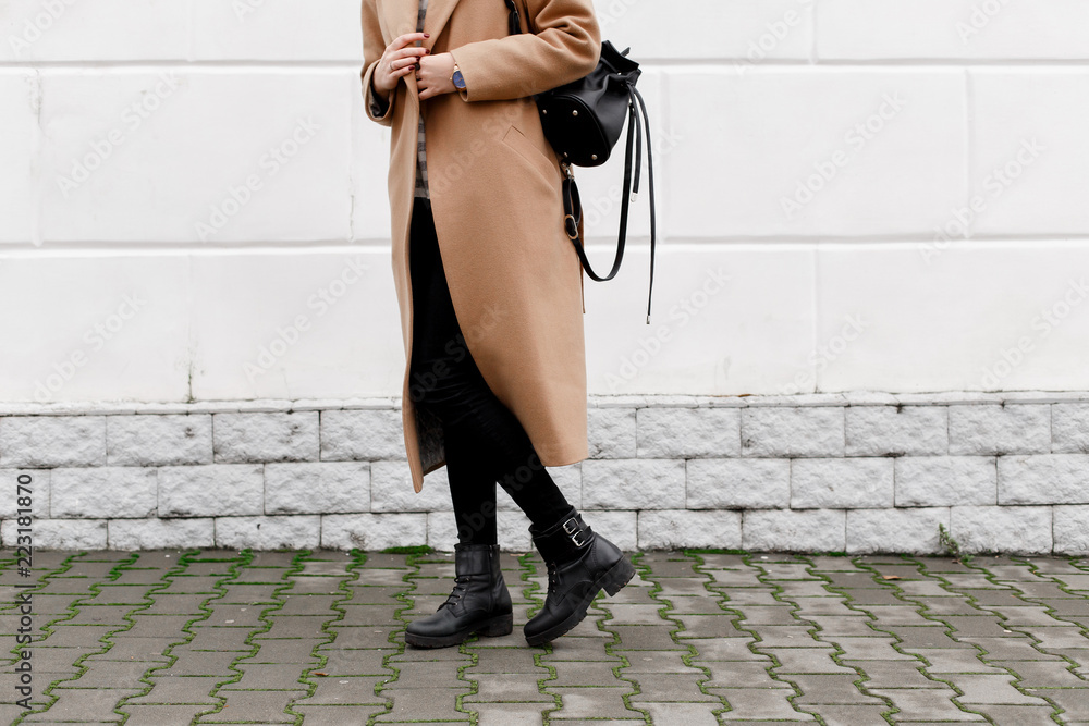 Women's legs. Woman wearing long beige coat, black boots and leather  backpack walking through the city streets. Trendy casual outfit. Details of  everyday look. Street fashion. Photos | Adobe Stock