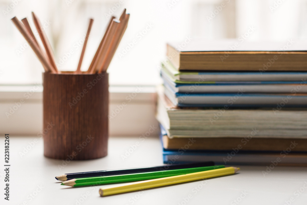 A stack of old books and several different colored pencils lie on the windowsill, a couple of pencils lie ahead A stack of old books and several different colored pencils lie on the windowsill, a couple of pencils lie ahead