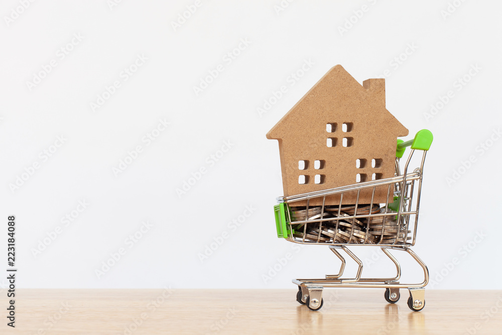 House model in mini shopping cart with stack of coins money on wooden table for residential investment. Concept for property ladder, mortgage and real estate investment
