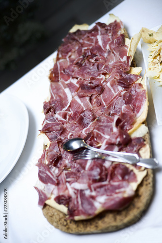 Vassoio di prosciutto tagliato finemente a fette sopra una sfoglia di pane carasau in un vassoio di sughero