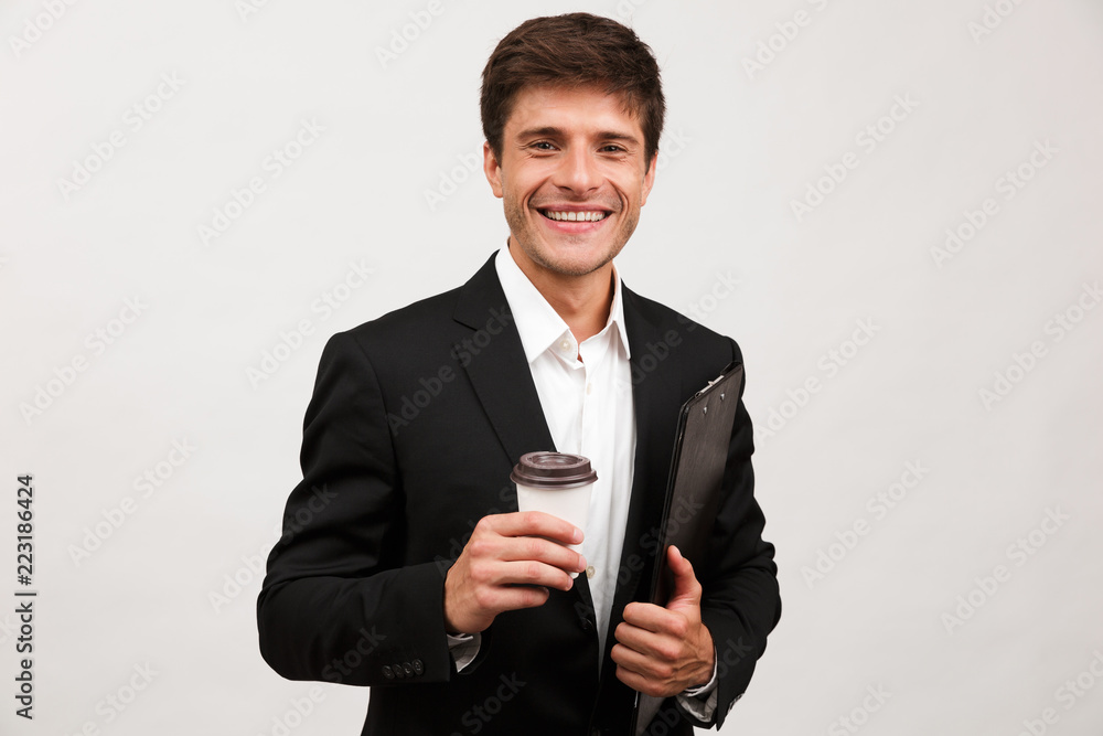 Businessman standing isolated holding clipboard looking camera drinking coffee. Businessman standing isolated holding clipboard looking camera drinking coffee.