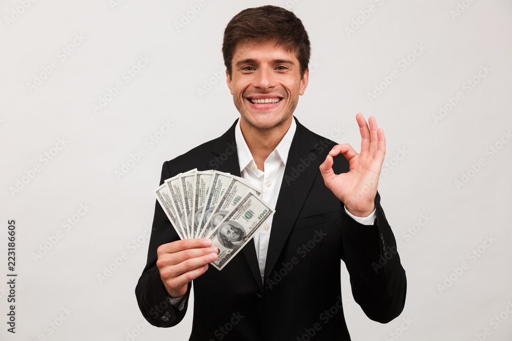 Happy businessman standing isolated holding money make okay gesture. Happy businessman standing isolated holding money make okay gesture.