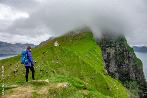 Unrecognizable female hiker stands on top of hill and looks towards lighthouse. © helivideo