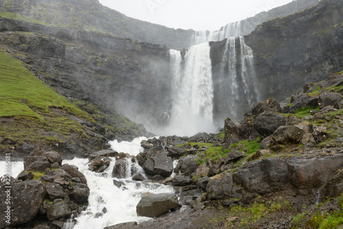 Spectacular mountain stream splashes over the rocky cliff  creating a waterfall.