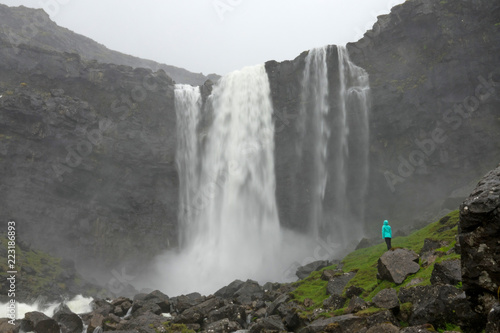 Young female hiker observes the spectacular waterfall in scenic Faroe Islands.