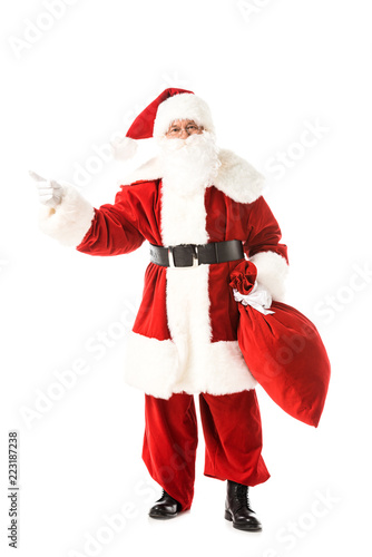 santa claus holding sack and pointing away while looking at camera isolated on white