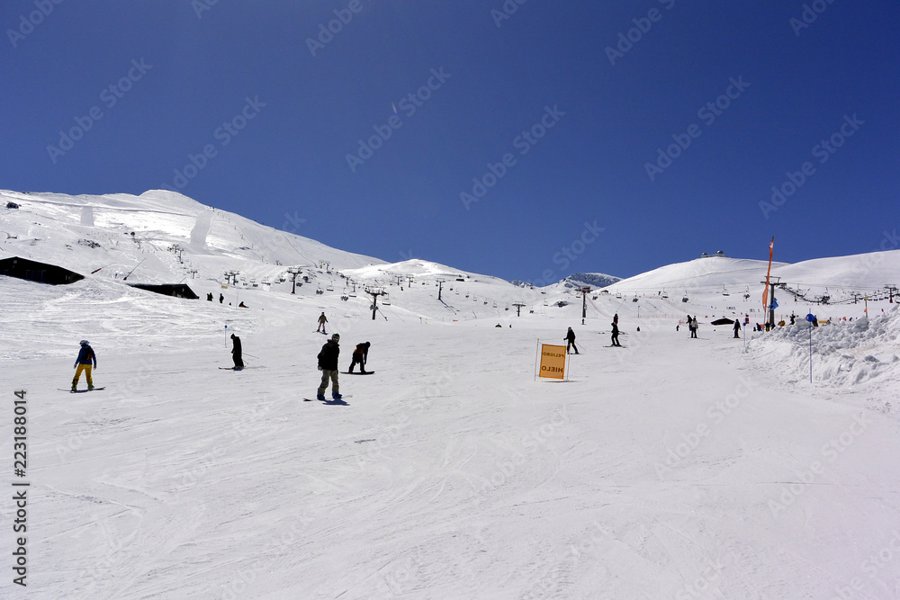 White snow-capped mountain slopes with skiers and blue sky with white clouds