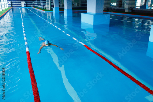 Photo on top of sportive man in blue cap swimming on path in pool under water