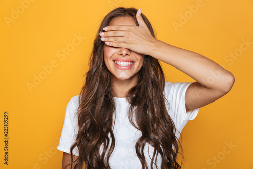Fotografie Image of excited woman 20s with long hair smiling and covering eyes with hands,