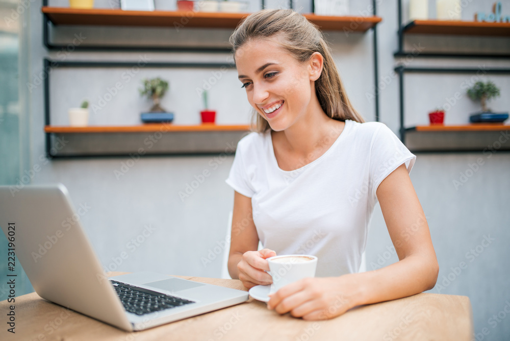 Smiling girl looking at laptop while drinking cappuccino. Smiling girl looking at laptop while drinking cappuccino.