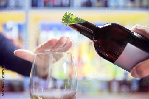 Woman hand rejecting more alcohol from wine bottle in bar photo