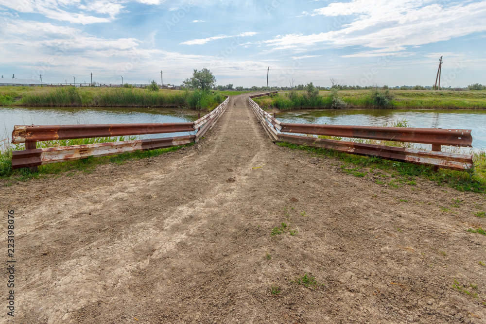 The perspective view through the small rural bridge on the river in the fields The perspective view through the small rural bridge on the river in the fields