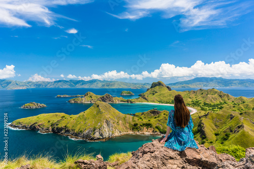 Rear view of a young woman enjoying the awesome view of Padar Island, while sitting on the top of a volcanic mountain during summer vacation in Indonesia photo