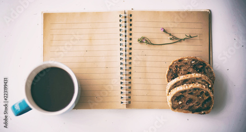 The blurry light design background of  blue ceramic coffee cup with black coffee put beside book and mixed fruit bread,on white desk,vintage and art tone