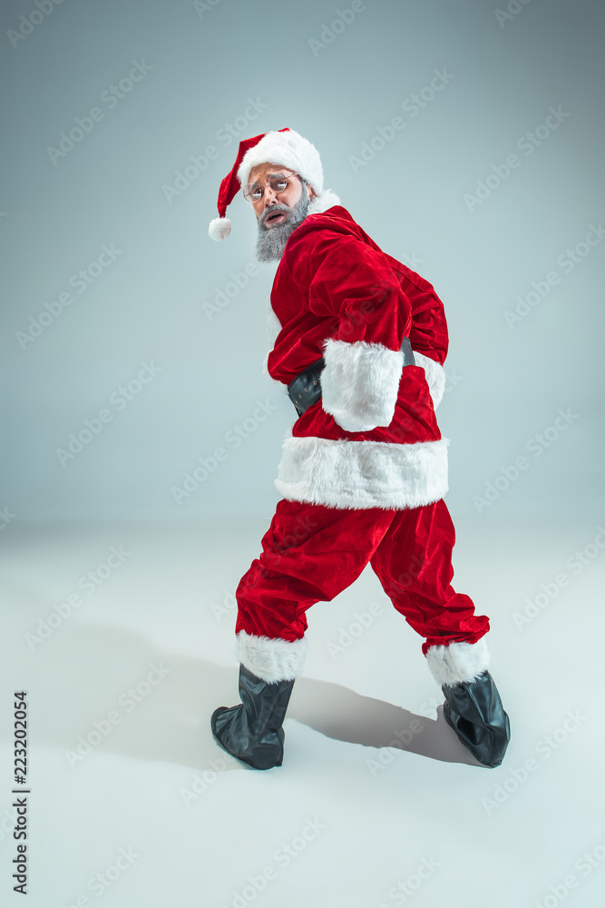 Funny serious guy with christmas hat dancing at studio. New Year Holiday. Christmas, x-mas, winter, gifts concept. Man wearing Santa Claus costume on gray. Copy space. Winter sales. Funny serious guy with christmas hat dancing at studio. New Year Holiday. Christmas, x-mas, winter, gifts concept. Man wearing Santa Claus costume on gray. Copy space. Winter sales.