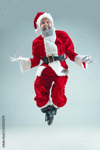 Funny serious guy with christmas hat dancing at studio. New Year Holiday. Christmas, x-mas, winter, gifts concept. Man wearing Santa Claus costume on gray. Copy space. Winter sales. © master1305